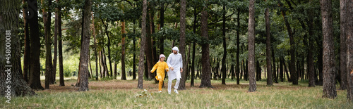 Smiling muslim father and son running in park, banner