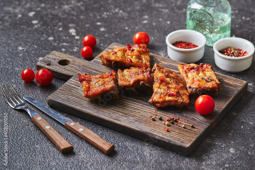 Grilled baked pork ribs with spices and vegetables on wooden cutting board on dark background. American food concept.