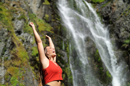 Woman raising arms in a waterfall celebrating holiday