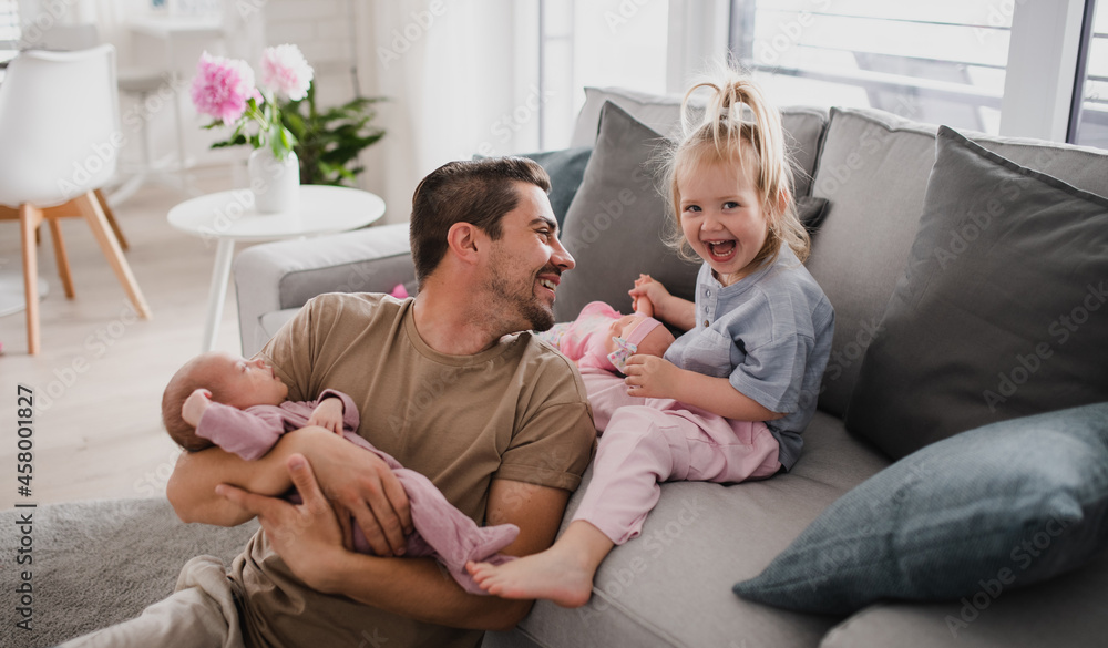 Happy young man taking care of his newborn baby and little daughter indoors at home, paternity leave. Happy young man taking care of his newborn baby and little daughter indoors at home, paternity leave.