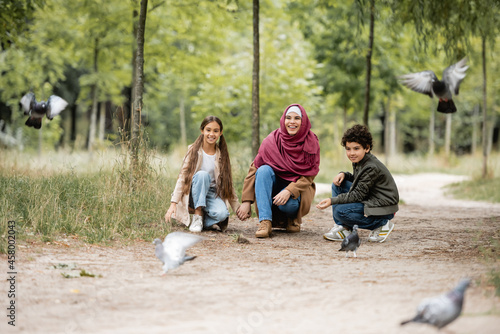 Canvas Print Smiling muslim woman and children looking at blurred birds in park