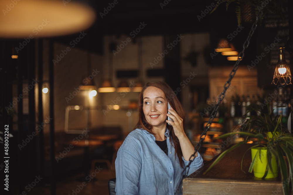 Obraz premium middle-aged woman in a blue shirt uses a mobile phone in a cafe