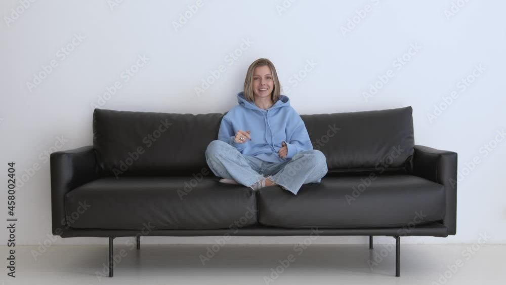 Smiling and cheerful woman in casual clothes talking, looking at the camera, with legs on a couch. Caucasian woman giving a talk on a video camera at home interior Smiling and cheerful woman in casual clothes talking, looking at the camera, with legs on a couch. Caucasian woman giving a talk on a video camera at home interior