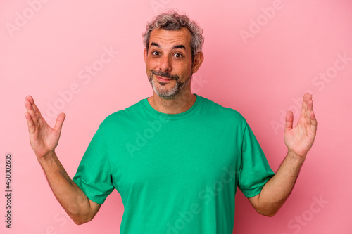 Middle age caucasian man isolated on pink background holding something little with forefingers, smiling and confident.