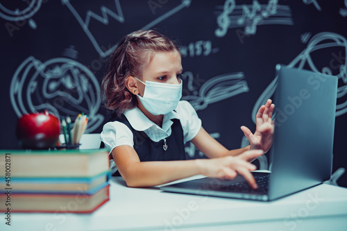 Junior student wearing medical mask online virtual learning language class on laptop.