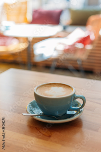 Cup of cappuccino with latte art. Coffee in blue cup on wooden table in cafe. Concept of easy breakfast.