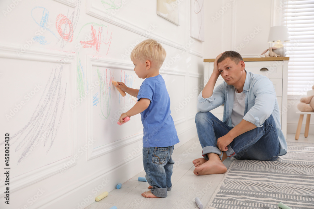 Upset father watching his little son drawing on wall at home - obrazy, fototapety, plakaty 