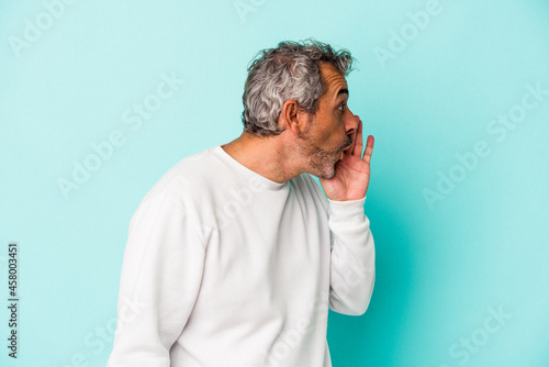 Middle age caucasian man isolated on blue background is saying a secret hot braking news and looking aside