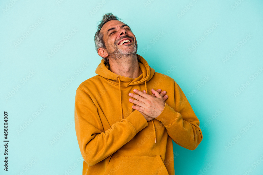 Middle age caucasian man isolated on blue background  laughing keeping hands on heart, concept of happiness.