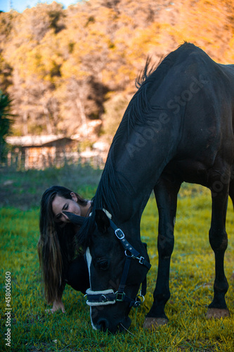 Young girl with horse at summer evening day, sunset light, sitting and resting in the field © Laia