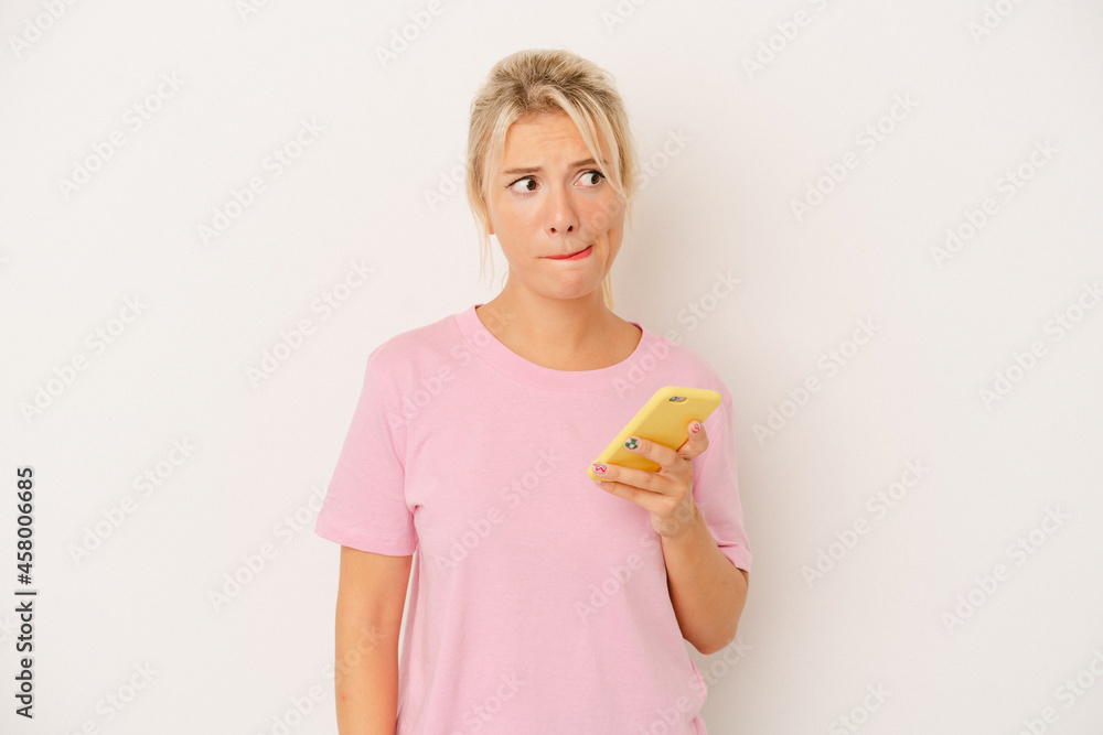 Young Russian woman holding mobile phone isolated on white background confused, feels doubtful and unsure. Young Russian woman holding mobile phone isolated on white background confused, feels doubtful and unsure.