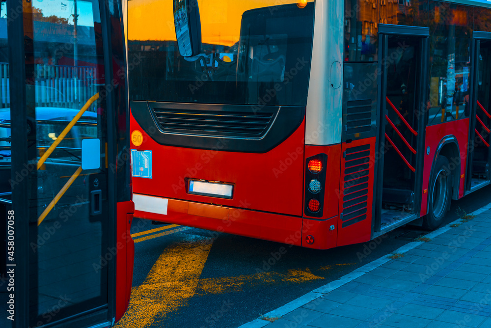 Two red bus on buses stop at city street on evening time of the day