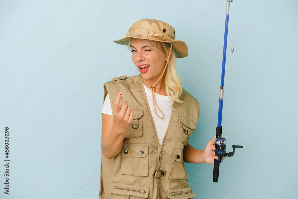 Young Russian fisherwoman isolated on blue background pointing with finger at you as if inviting come closer. Young Russian fisherwoman isolated on blue background pointing with finger at you as if inviting come closer.