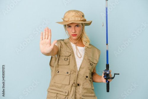 Young Russian fisherwoman isolated on blue background standing with outstretched hand showing stop sign, preventing you.