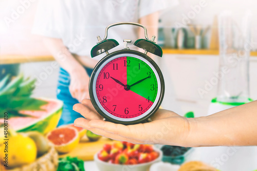 Hand holding a clock in a kitchen. Intermittent fasting concept.  Empty copy space for Editor's text.