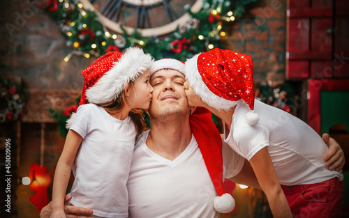 Single dad with two children at christmas time. Children in red Christmas caps are enjoying Christmas with their dad. Children kiss their parent.