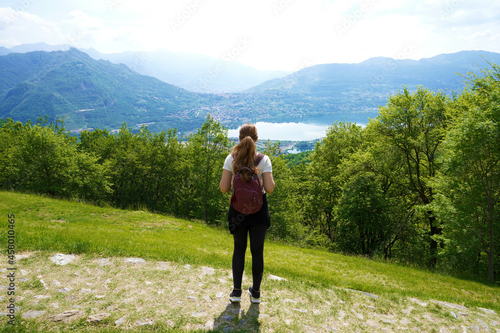 Female hiker standing on the trail and looks with satisfaction from the top of mountain the lake