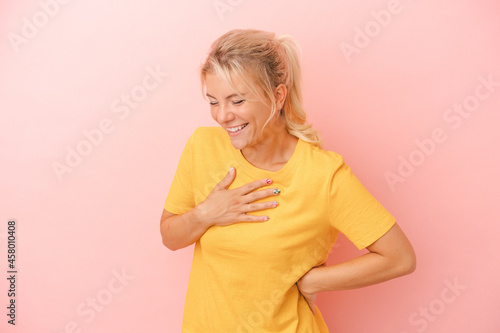 Young Russian woman isolated on pink background laughing keeping hands on heart, concept of happiness.