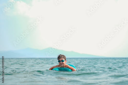Little boy with inflatable inner tube having fun in the clean sea.