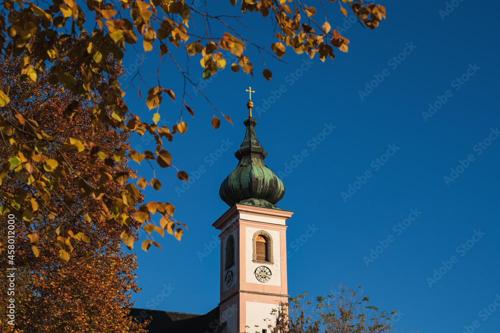 Selective focus on the church tower of Aigen with autumn colored trees in Salzburg, Austria