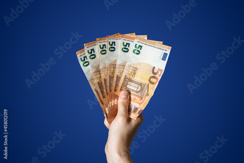 Hand holding three hundred euros in 50 euro bills with blue background