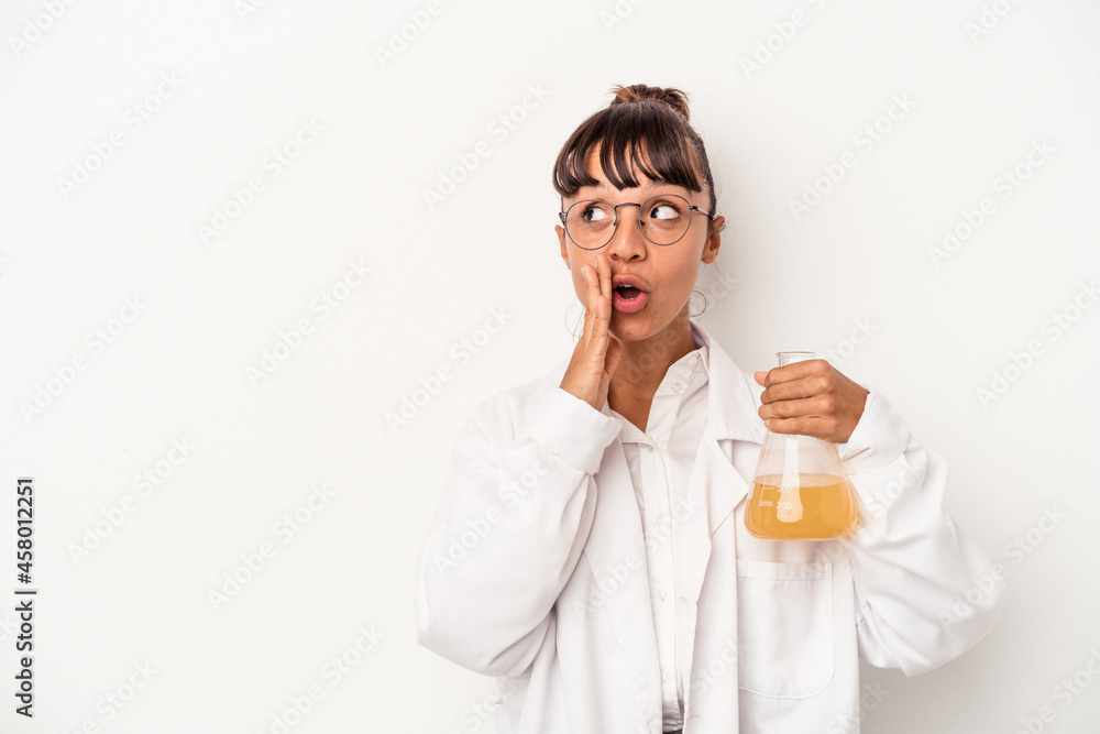 Young mixed race scientist woman holding a test tube isolated on white background is saying a secret hot braking news and looking aside Young mixed race scientist woman holding a test tube isolated on white background is saying a secret hot braking news and looking aside