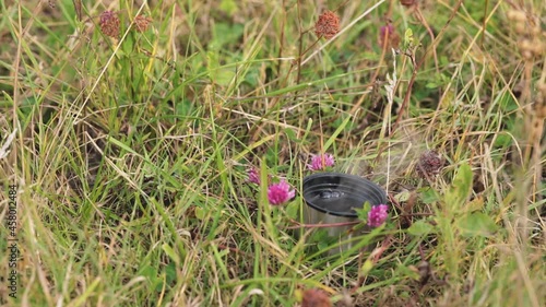 The tourist poured hot coffee from a thermos into the lid of the thermos and put it on the grass. Travel accessories. Morning drink outdoors. Travel videos.