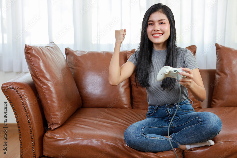 VDO game console station concept. active asian woman sitting on sofa, holding joystick and playing exciting game. Cute girl looked excited with game controller console VDO game console station concept. active asian woman sitting on sofa, holding joystick and playing exciting game. Cute girl looked excited with game controller console