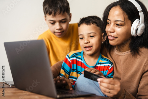 Mother with tow sons smiling and using laptop and credit card