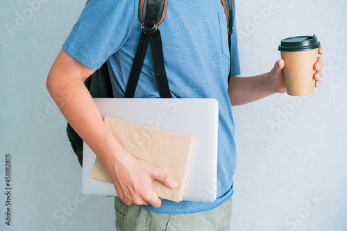 Teenager with backpack, textbooks and laptop on light background
