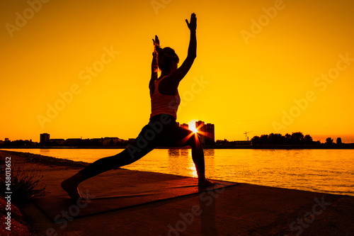 Young woman is exercising outdoor. She is practicing yoga on sunny day. Virabhadrasana   Variation of Warrior pose.