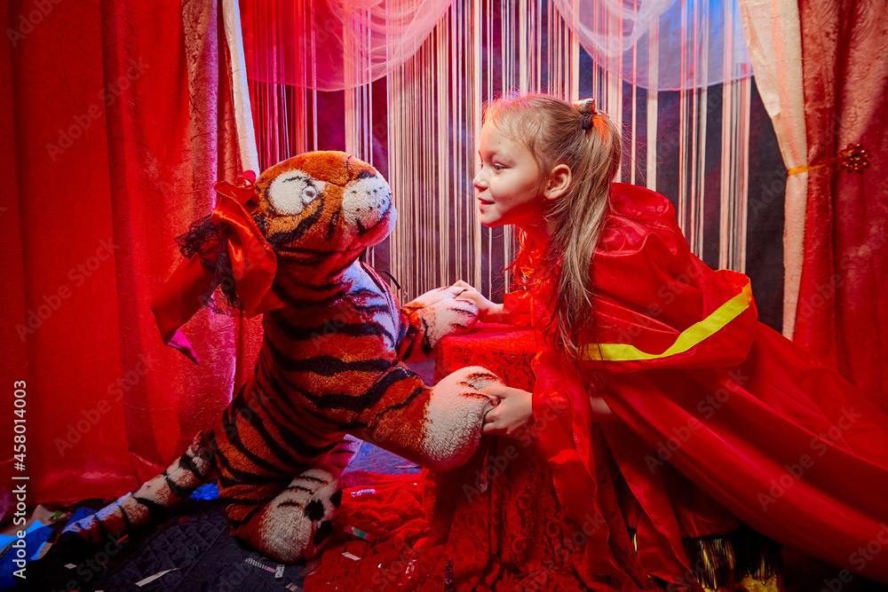 Small girl during a stylized theatrical circus photo shoot in a beautiful red location. Young model posing on stage with curtain Small girl during a stylized theatrical circus photo shoot in a beautiful red location. Young model posing on stage with curtain