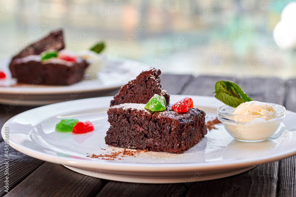 Slice of chocolate cake with candied fruit, mint and ice cream on a white plate and wooden background Slice of chocolate cake with candied fruit, mint and ice cream on a white plate and wooden background