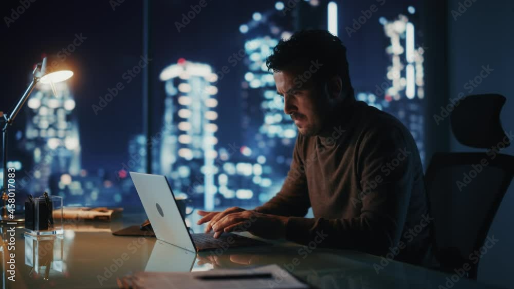 Portrait of Thoughtful Successful Businessman Working on Laptop Computer in His Big City Office at Night. Charismatic Digital Entrepreneur does Data Analysis for e-Commerce Strategy. Medium Shot Portrait of Thoughtful Successful Businessman Working on Laptop Computer in His Big City Office at Night. Charismatic Digital Entrepreneur does Data Analysis for e-Commerce Strategy. Medium Shot