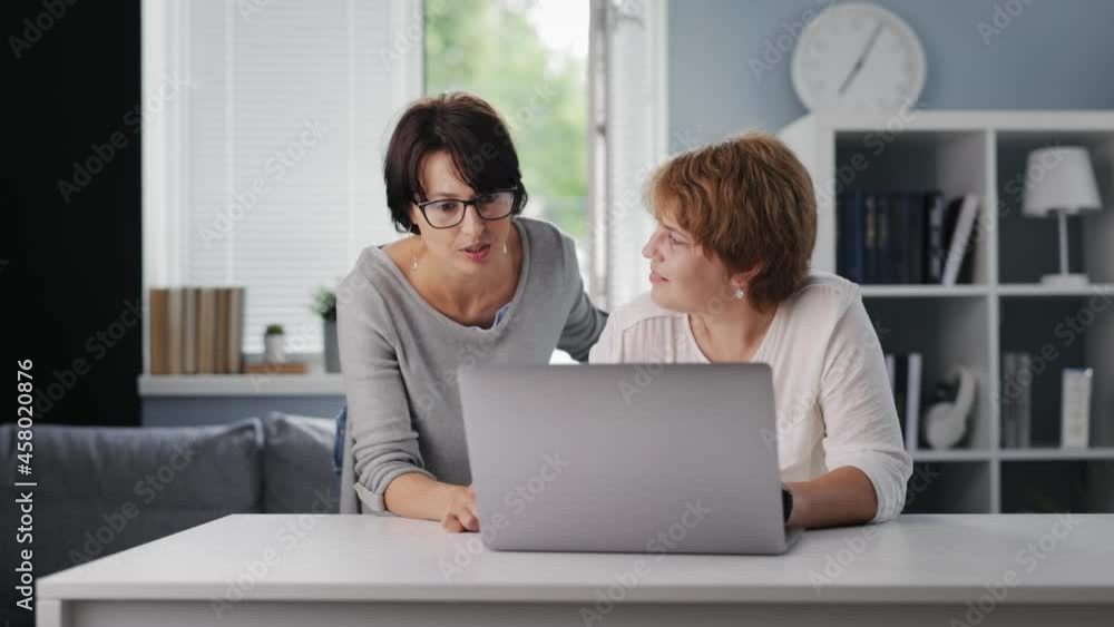 Beautiful mature woman in eyeglasses explaining her elder mother how to use wireless laptop. Caucasian daughter explaining parent about convenience of modern technology.