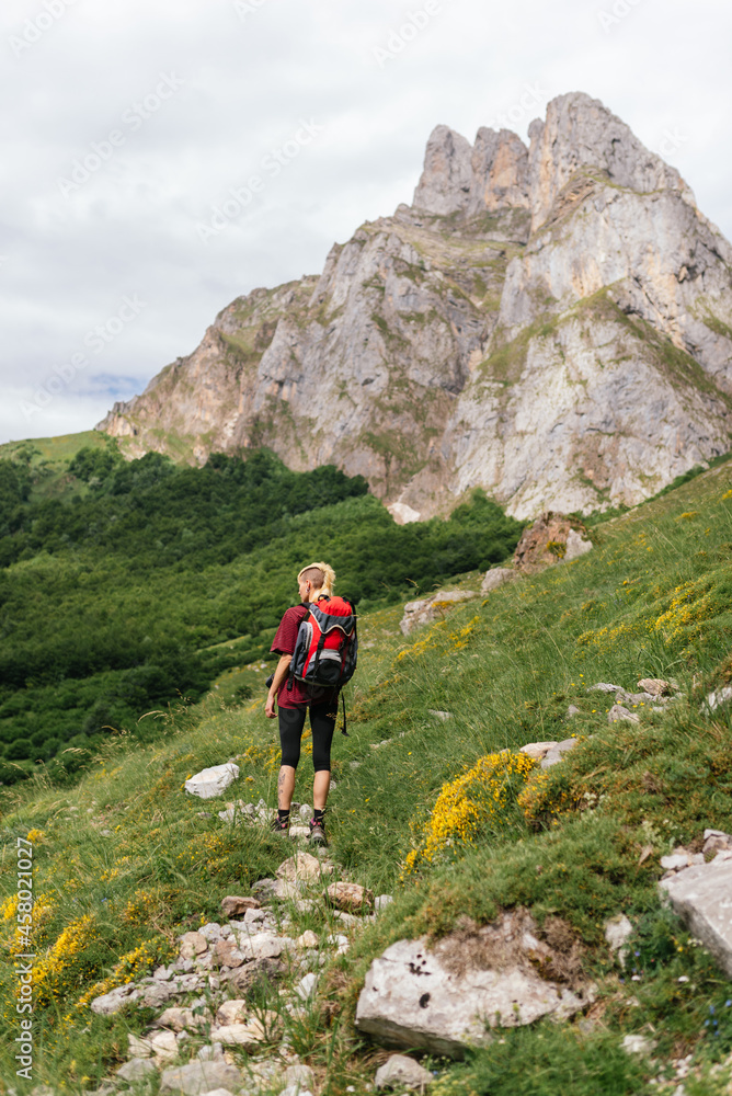 Young female traveler, with a backpack on her back, ascending a mountain during an excursion through the Picos de Europa National Park.