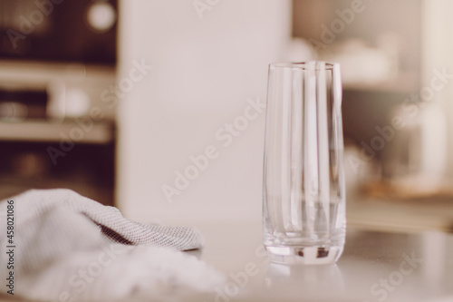 Transparent high empty glass on kitchen table. Natural day light reflections