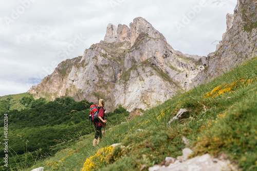 Young traveler woman, with a backpack on her back, ascending a mountain during an excursion through the Picos de Europa National Park.