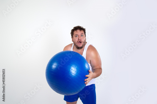 Funny fat man training with a fitness ball. Adult guy on a white background. Copy space. Active sports with a diet.   © Denis