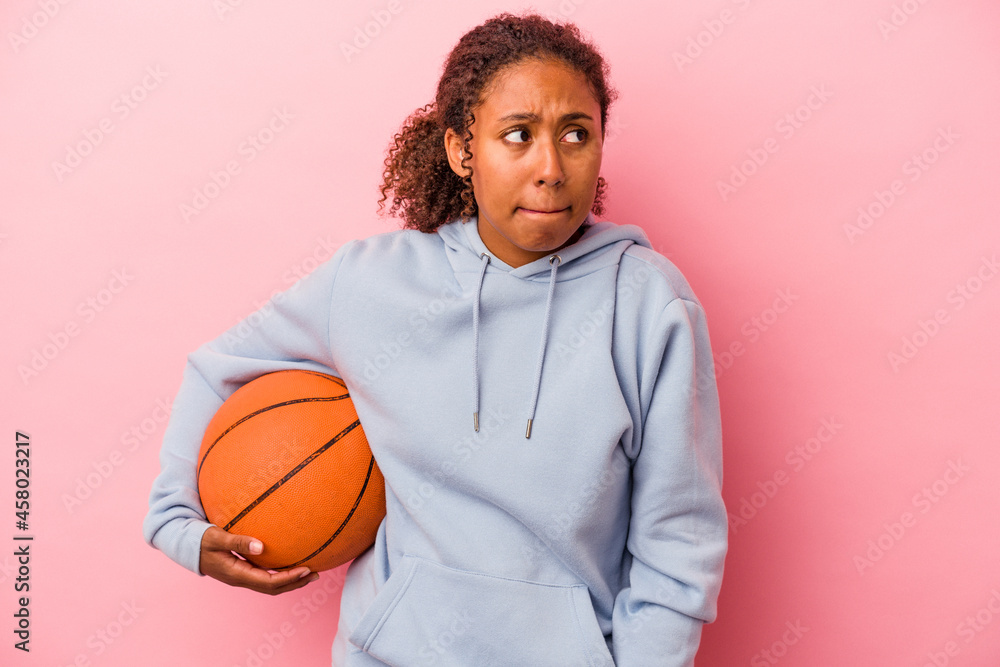 Young african american man playing basketball isolated on pink background confused, feels doubtful and unsure.