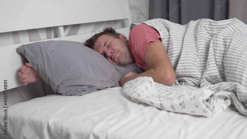 In the morning, the man sleeps soundly in bed alone. A sleepy dude stretches in bed and covers his head with a pillow. In the morning, the man sleeps soundly in bed alone. A sleepy dude stretches in bed and covers his head with a pillow.
