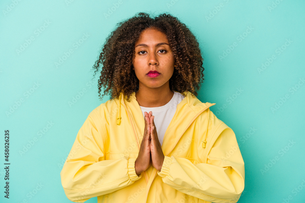 Young african american woman with curly hair isolated on blue background praying, showing devotion, religious person looking for divine inspiration. Young african american woman with curly hair isolated on blue background praying, showing devotion, religious person looking for divine inspiration.