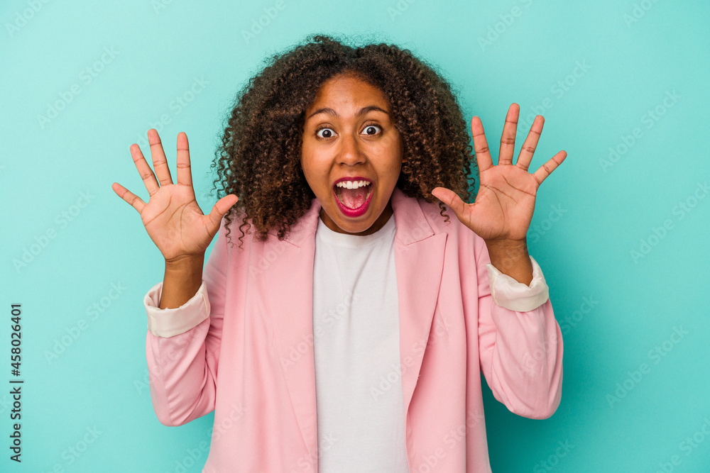 Young african american woman with curly hair isolated on blue background receiving a pleasant surprise, excited and raising hands. Young african american woman with curly hair isolated on blue background receiving a pleasant surprise, excited and raising hands.