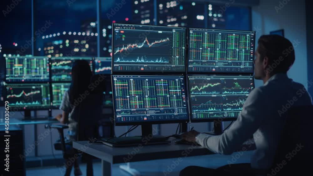 Financial Analyst Working on a Computer with Multi-Monitor Workstation with Real-Time Stocks, Commodities and Foreign Exchange Charts. Businessman Works in Investment Bank City Office at Night. Financial Analyst Working on a Computer with Multi-Monitor Workstation with Real-Time Stocks, Commodities and Foreign Exchange Charts. Businessman Works in Investment Bank City Office at Night.