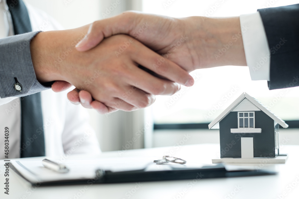 Businessmen and brokers' real estate agents shake hands after completing negotiations to buy houses insurance and sign contracts. Home insurance concept