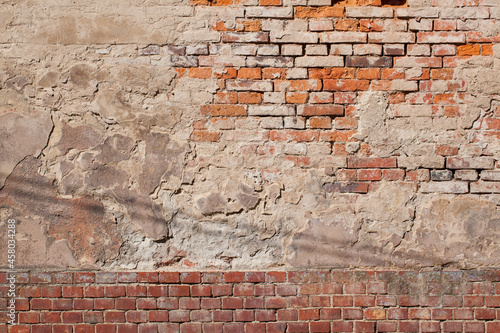 A fragment of an old  dingy brick wall along with remnants of plaster.