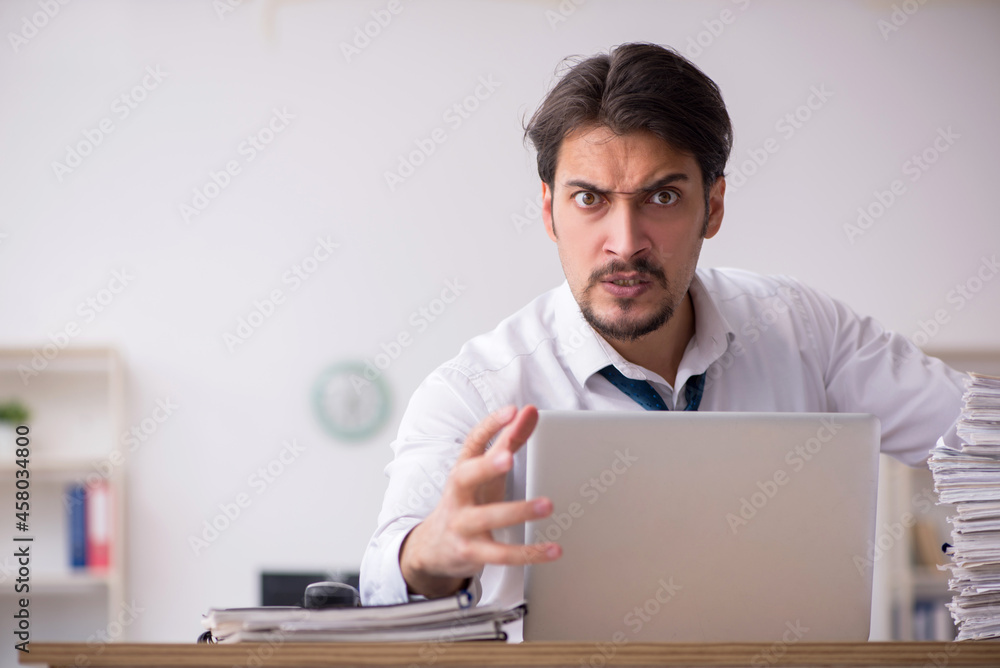 Young male employee unhappy with excessive work in the office Young male employee unhappy with excessive work in the office