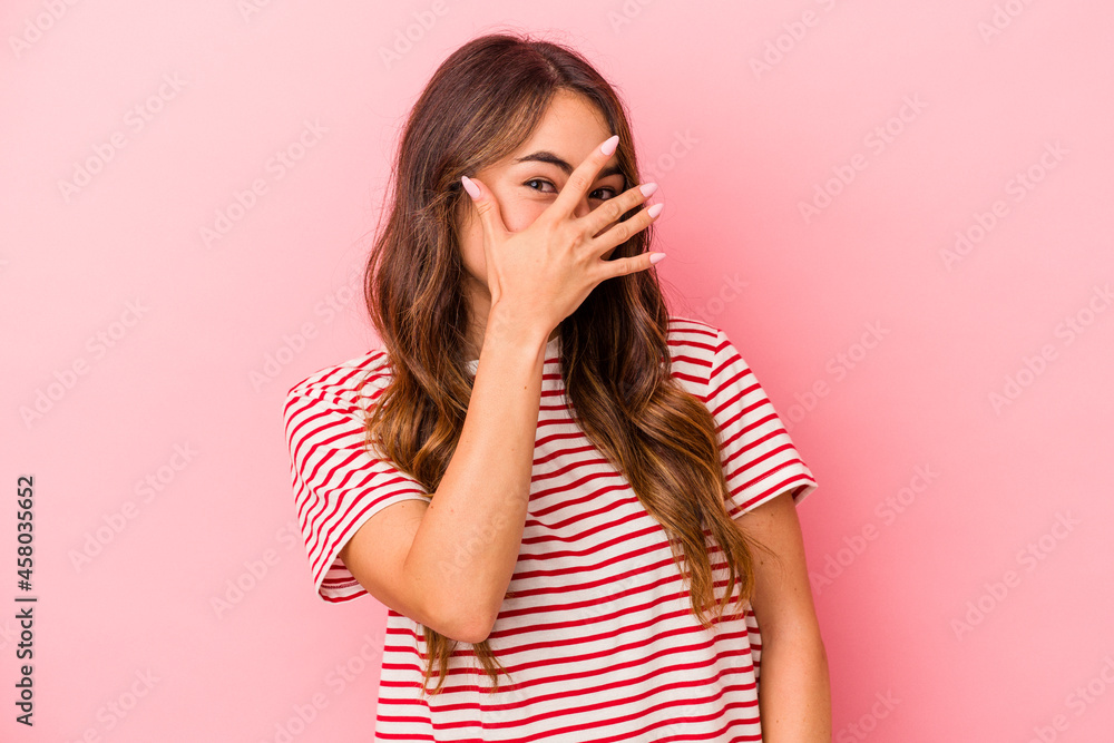 Young caucasian woman isolated on pink background blink at the camera through fingers, embarrassed covering face. Young caucasian woman isolated on pink background blink at the camera through fingers, embarrassed covering face.