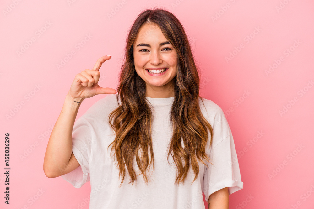 Young caucasian woman isolated on pink background holding something little with forefingers, smiling and confident. Young caucasian woman isolated on pink background holding something little with forefingers, smiling and confident.