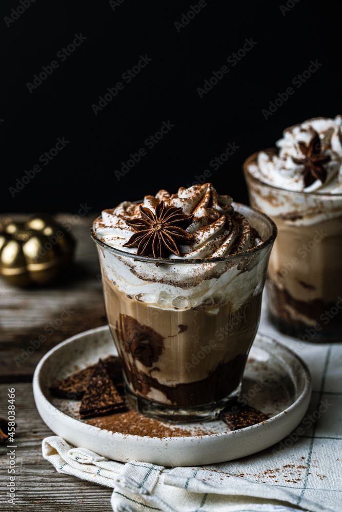Two glasses of Pumpkin pie spice mocha latte with whipped cream and dark chocolate on plate on wooden table on dark background . Two glasses of Pumpkin pie spice mocha latte with whipped cream and dark chocolate on plate on wooden table on dark background .